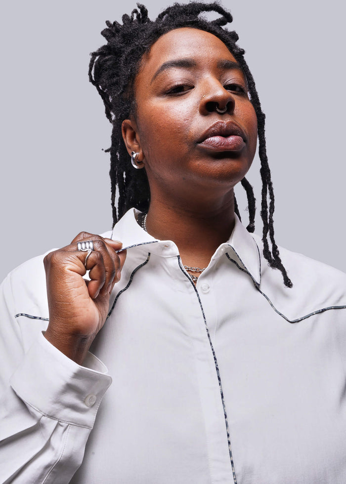 1X=Close up of person wearing a white shirt holding collar against a plain background