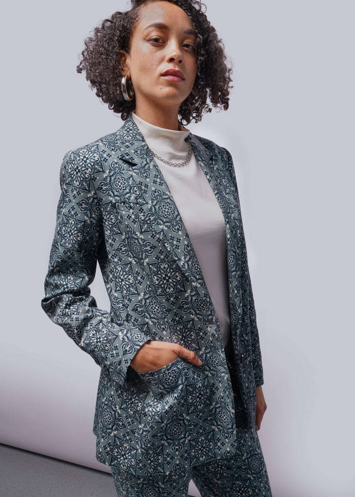 S=Person wearing a blue patterned suit with hand in pocket against a plain background