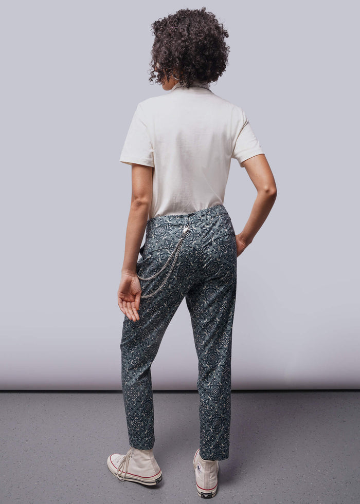 S=Person wearing a white shirt and patterned pants standing against a plain background