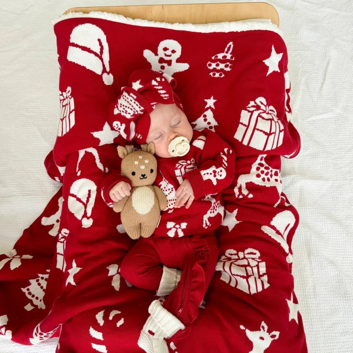 Baby in red pajamas with Christmas patterns lying on a matching red blanket.