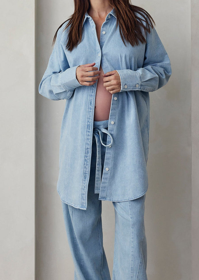 Person wearing a light blue denim shirt and pants against a plain background