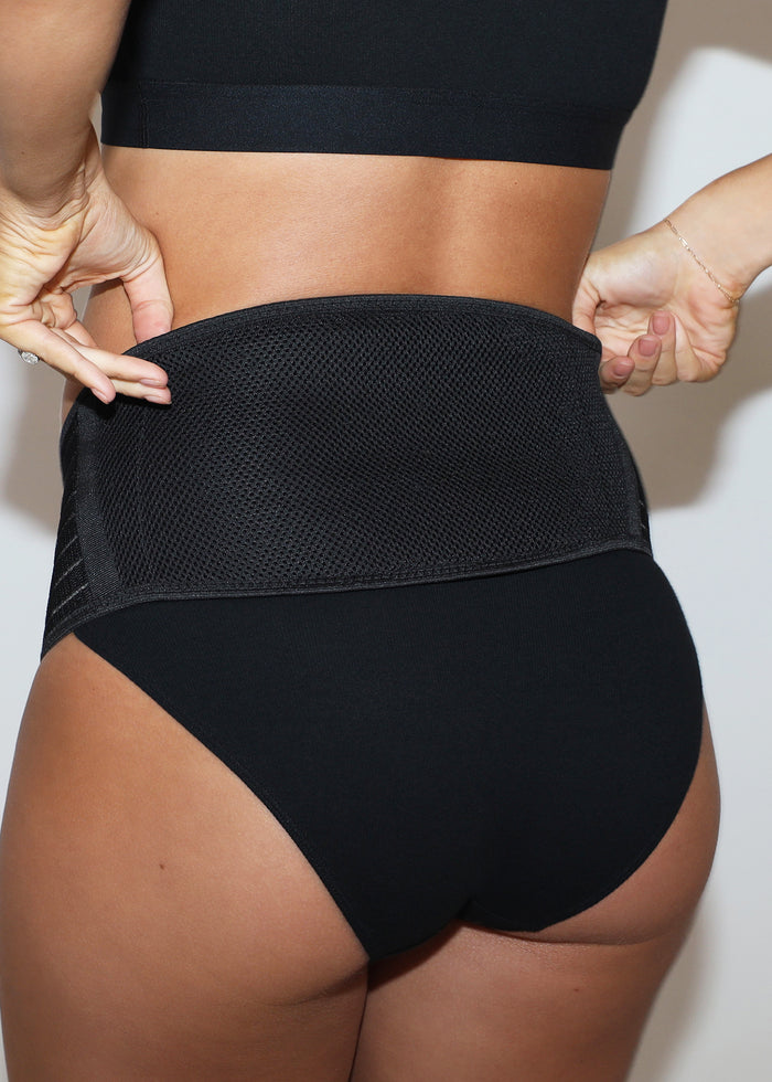 back view of a Pregnant model wearing underwear and  a belly support band in  black