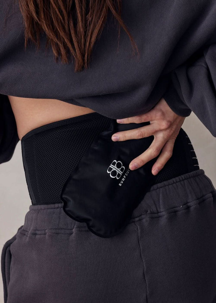model putting bumpsuit icepack on her lower back wearing a support band in black