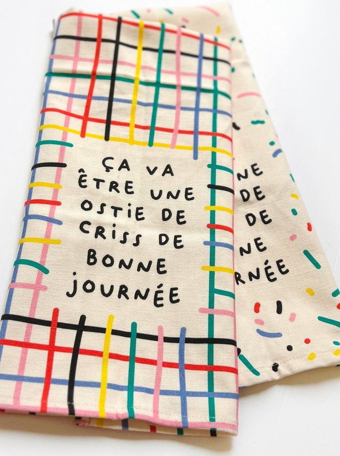 Linge à vaisselle rayé avec les couleurs primaires inscrit: ça va être une ostie de criss de bonne journée. Parfait idée cadeau pour femme. Fait au Québec.