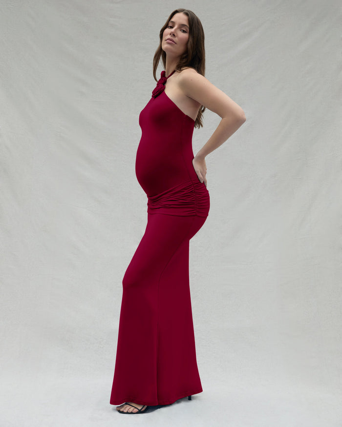 Pregnant woman wearing a burgundy dress against a plain background