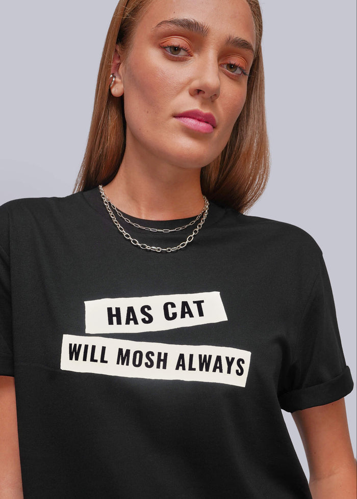 S=A woman wearing a black short-sleeve graphic t-shirt with white rectangular blocks containing the text 'HAS CAT' and 'WILL MOSH ALWAYS' in black capital letters. The background is a solid light gray studio backdrop.