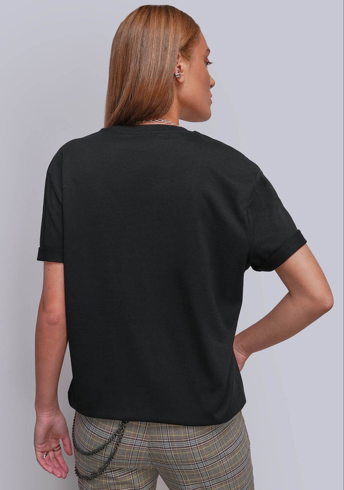 S=A woman shown from the back wearing a plain black short-sleeve t-shirt and beige plaid trousers, standing against a light gray studio background.