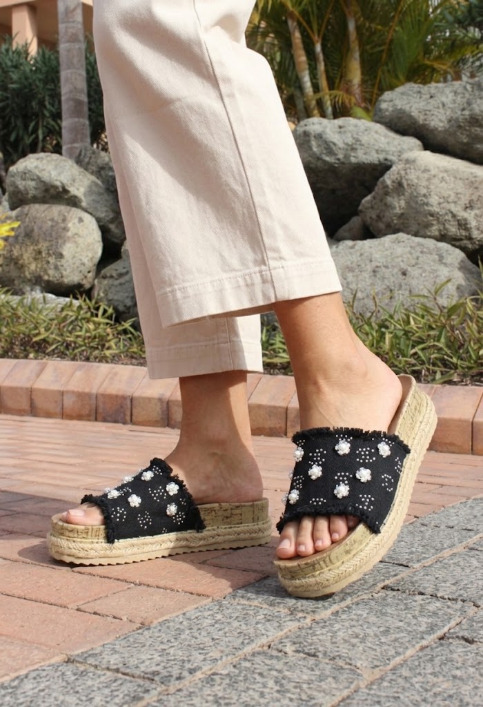 Person wearing black sandals with floral patterns on a stone path with rocks and plants in the background