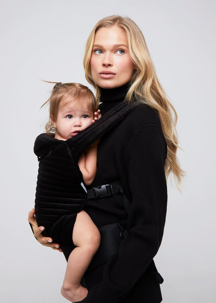 lady with baby wearing the bumpsuit armadillo baby carrier in black velvet