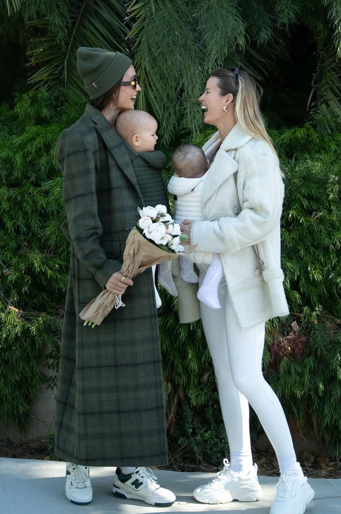 women laughing wearing their babies in the bumpsuit baby carriers in forest green and cloud colours