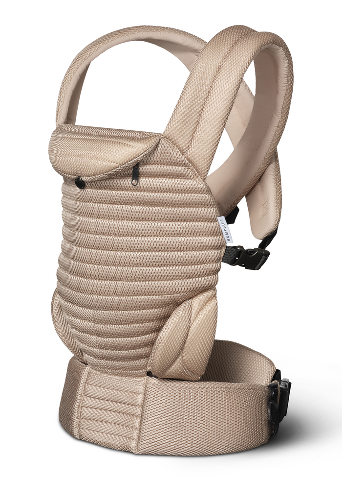 A tan mesh Bumpsuit armadillo baby carrier with a textured mesh fabric, padded shoulder straps, and black plastic buckle closures, shown against a plain white background.