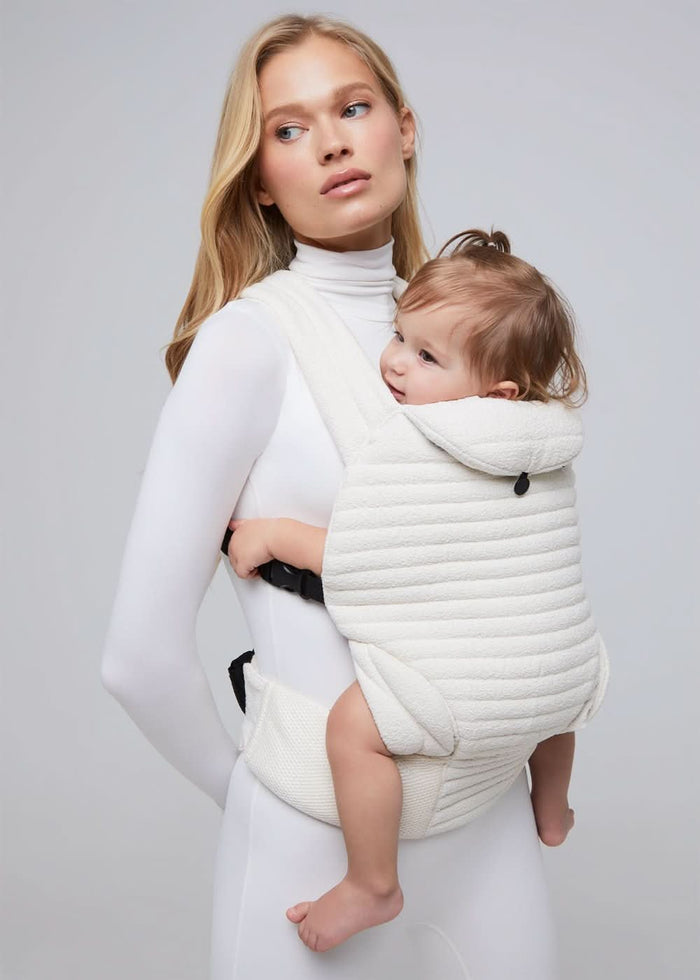 Model wearing an ivory coloured baby carrier with white background in bumpsuit one piece