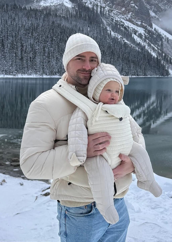 man in the snow wearing the bumpsuit baby career in ivory color
