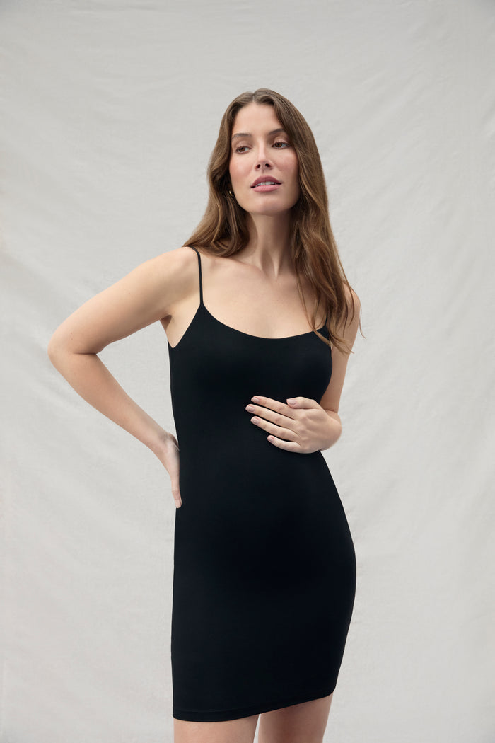 Woman wearing a  Bumpsuit Maternity mini black slip dress against a plain background