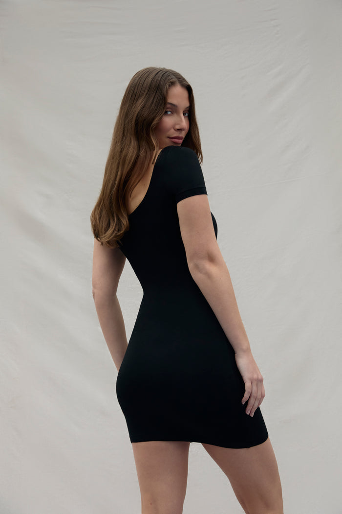 back view of a woman wearing a black Bumpsuit dress against a plain background