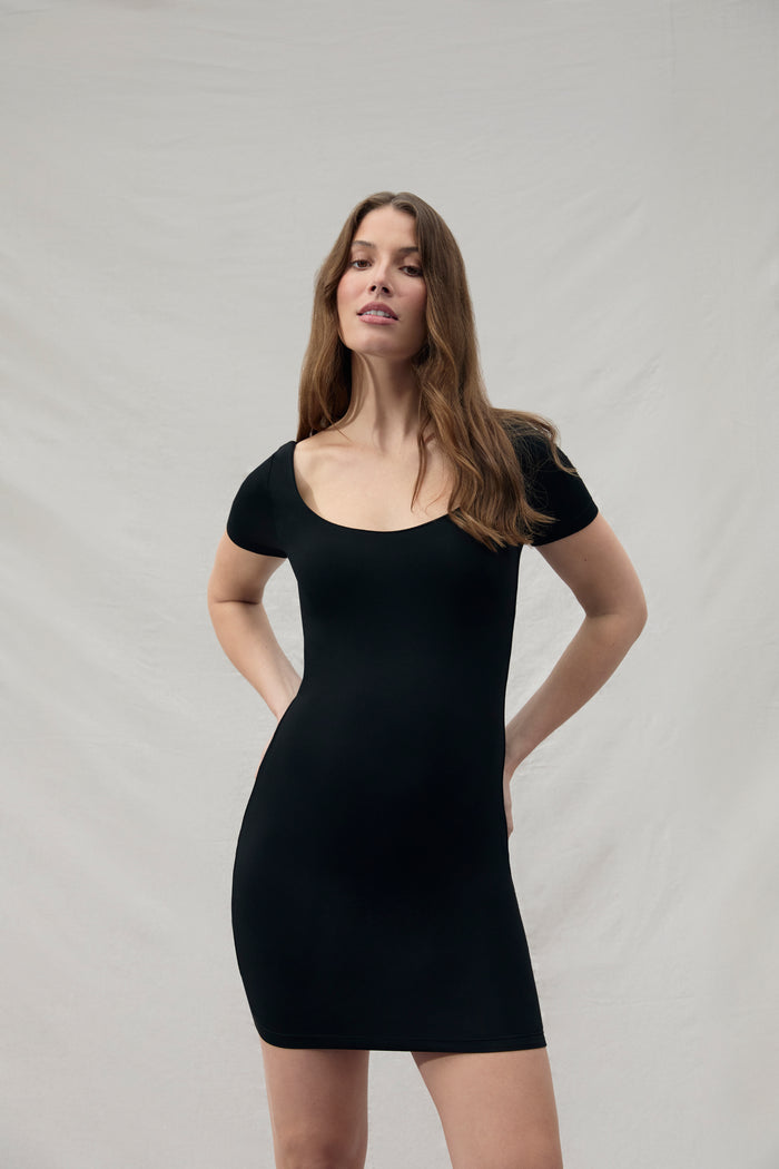 Woman wearing a mini black Bumpsuit dress against a plain background