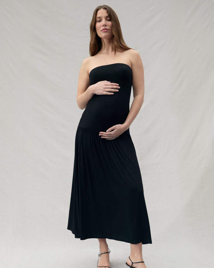 Pregnant woman wearing a black strapless dress on a plain background
