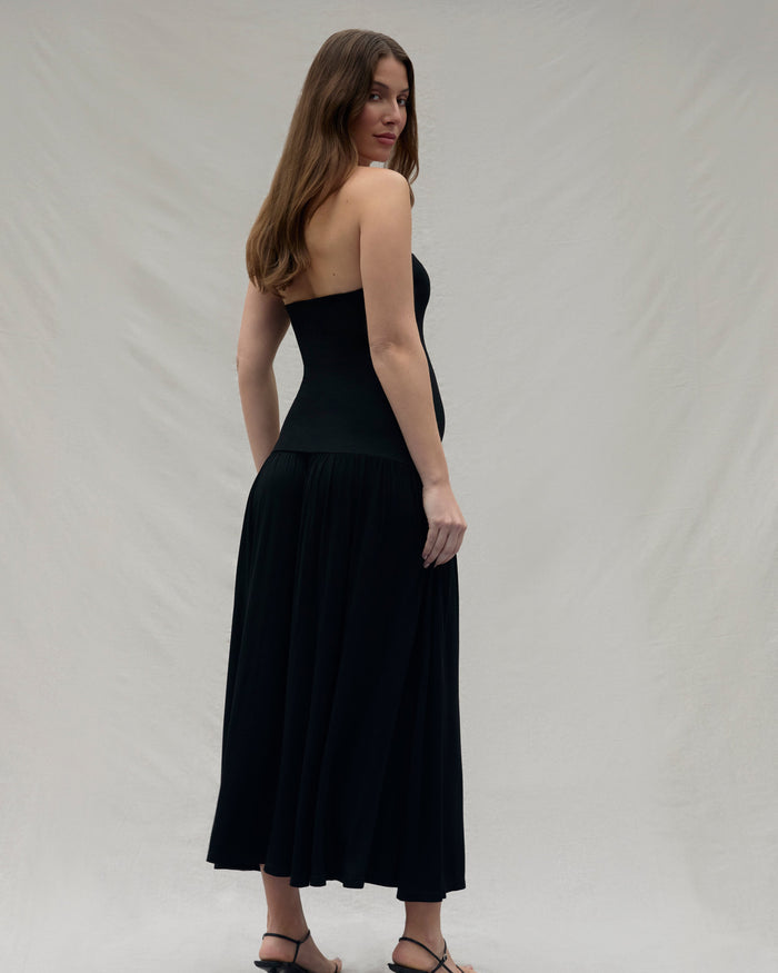 Woman wearing a black strapless dress against a plain background