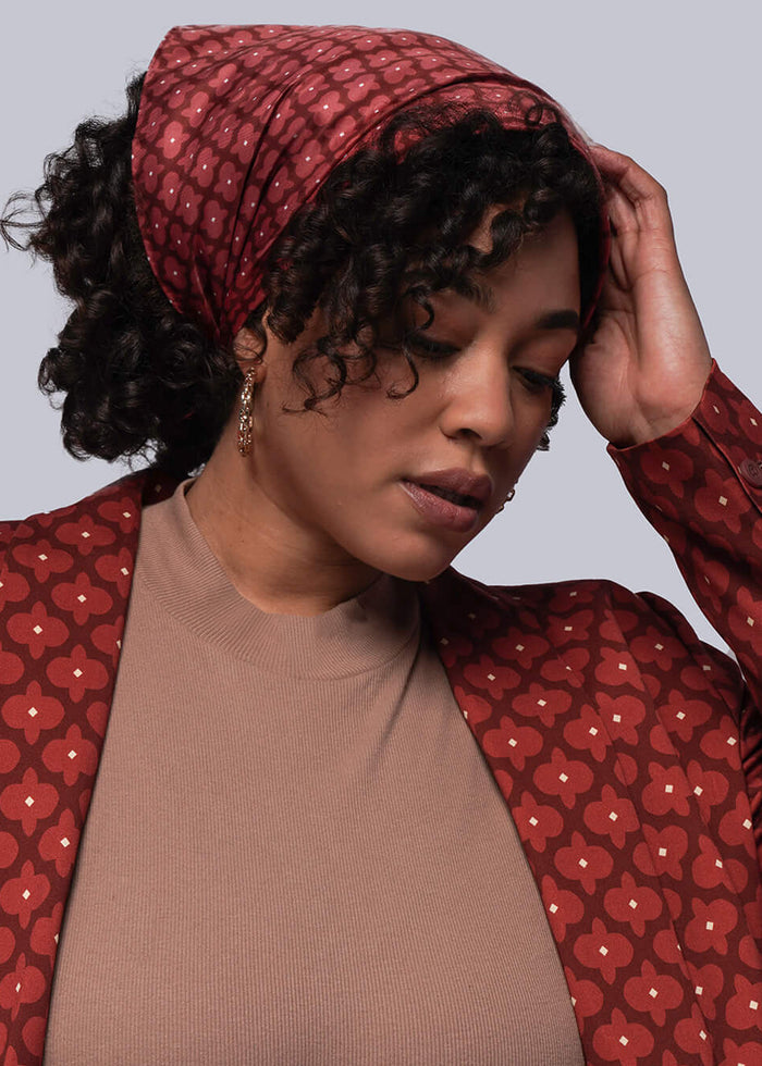Person wearing a red patterned jacket over a brown top and blue jeans on a gray background