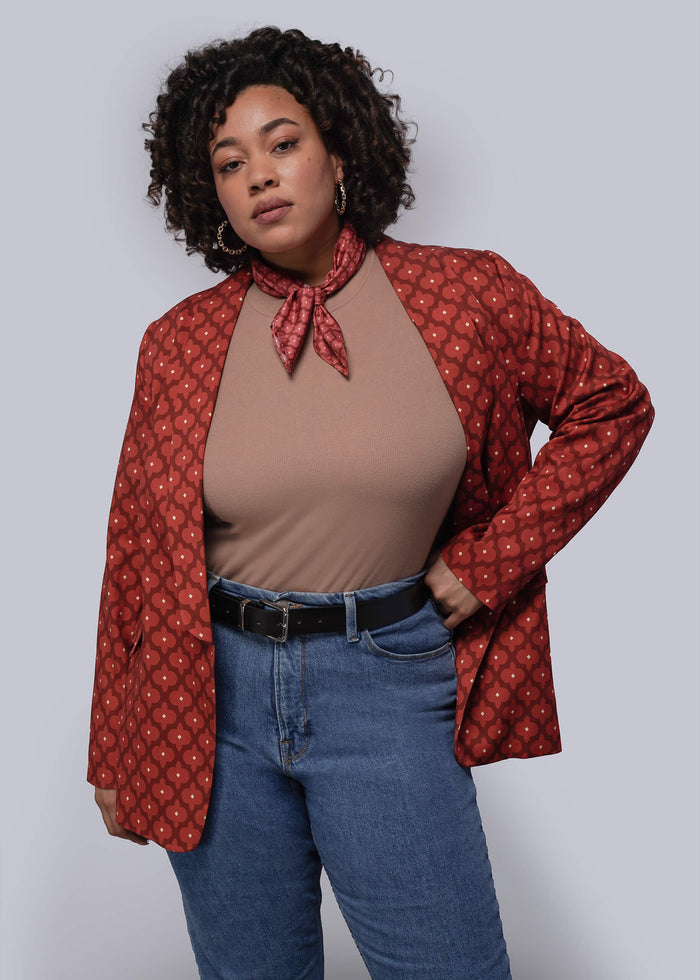 Person wearing a red patterned jacket over a brown top and blue jeans on a plain background