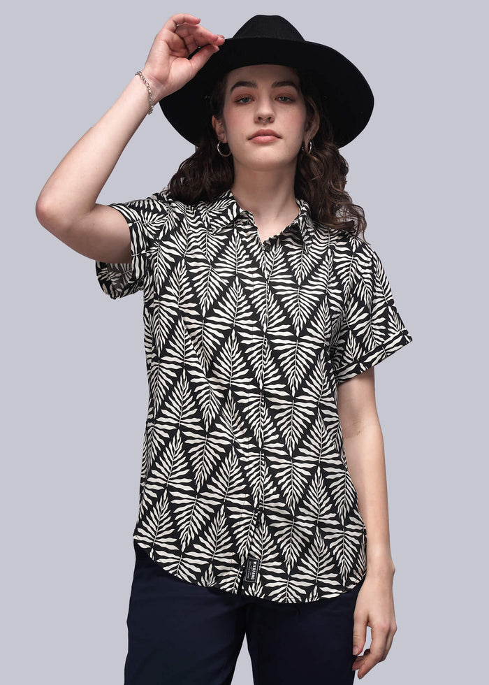 S=Woman wearing a black and white patterned blouse with a black hat on a gray background