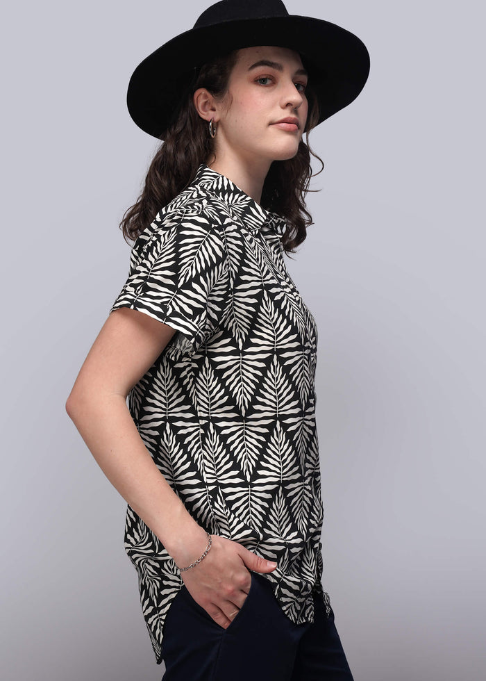 S=Woman wearing a black and white patterned shirt with a wide-brimmed hat on a gray background