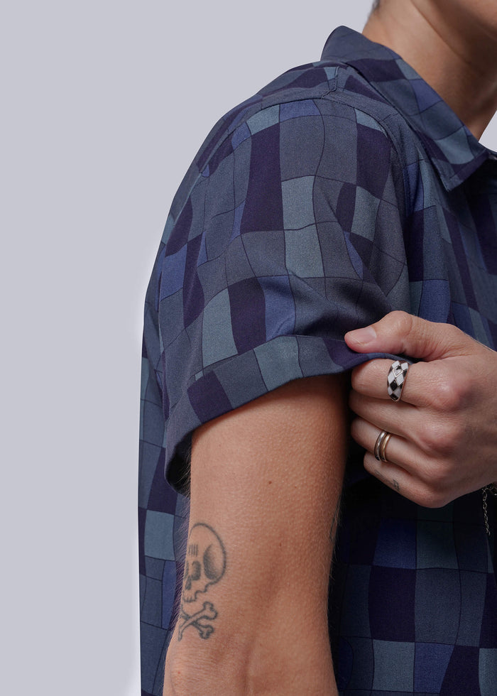 S=Close up of person wearing a blue checkered shirt showing the sleeve cuff with a plain background
