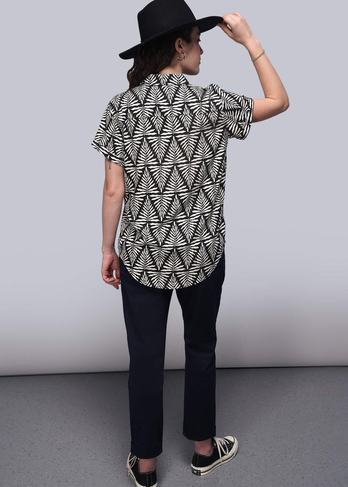 S=Person wearing a black and white patterned shirt with a black hat on a gray background