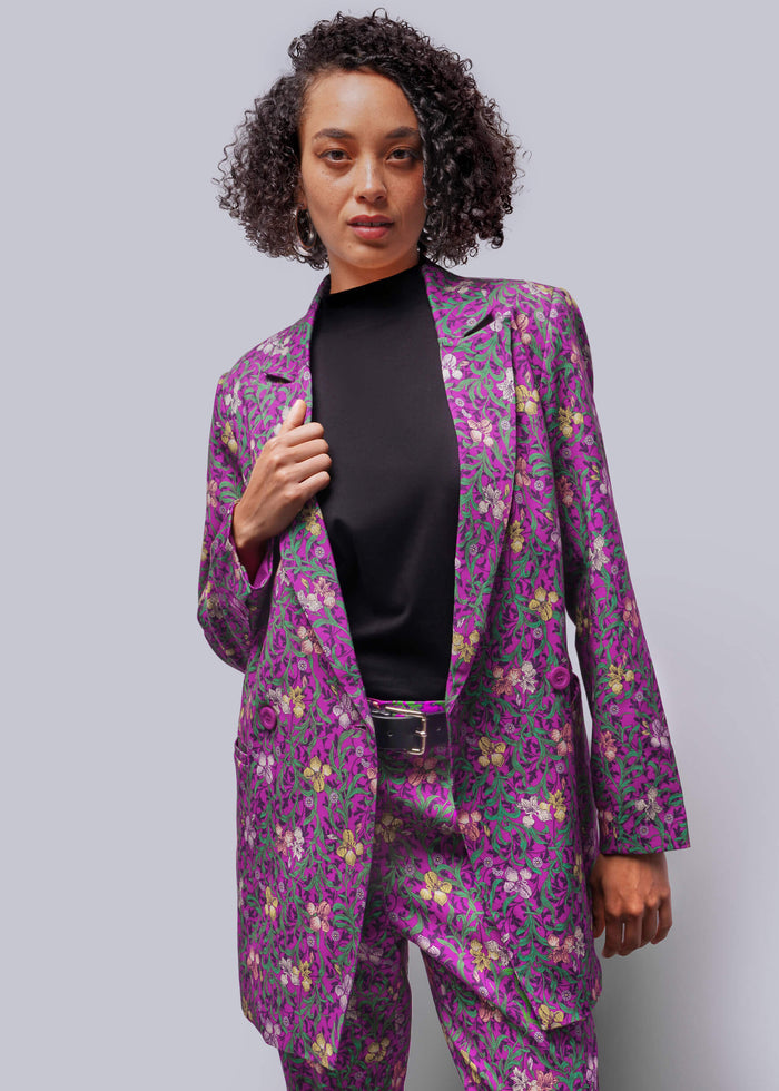 S=Woman wearing a purple floral suit against a gray background