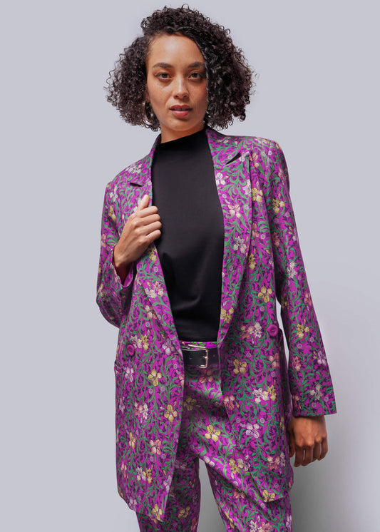 S=Woman wearing a purple floral suit against a gray background