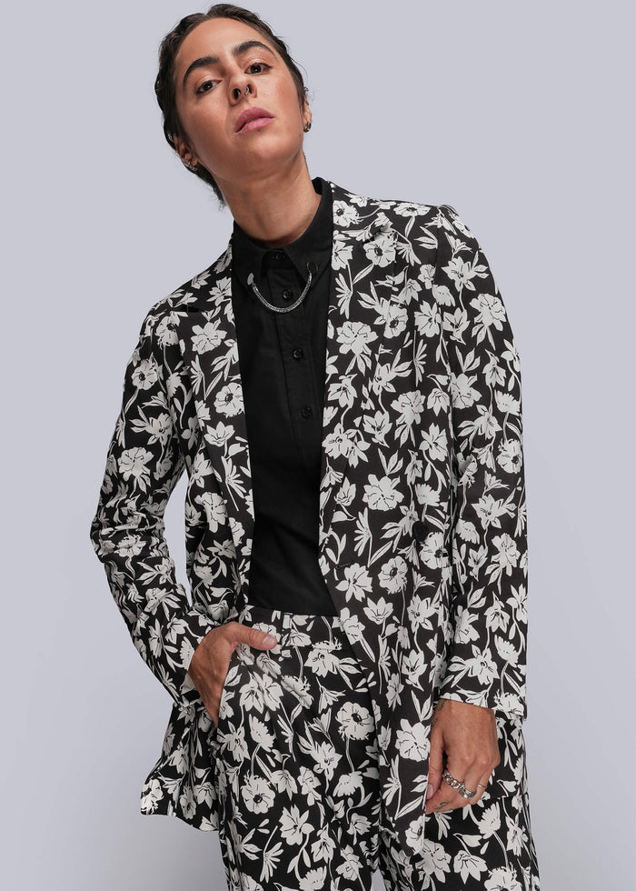 S=Person wearing a black and white floral suit against a gray background