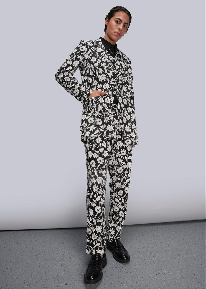 S=Person wearing a black and white floral suit against a plain background