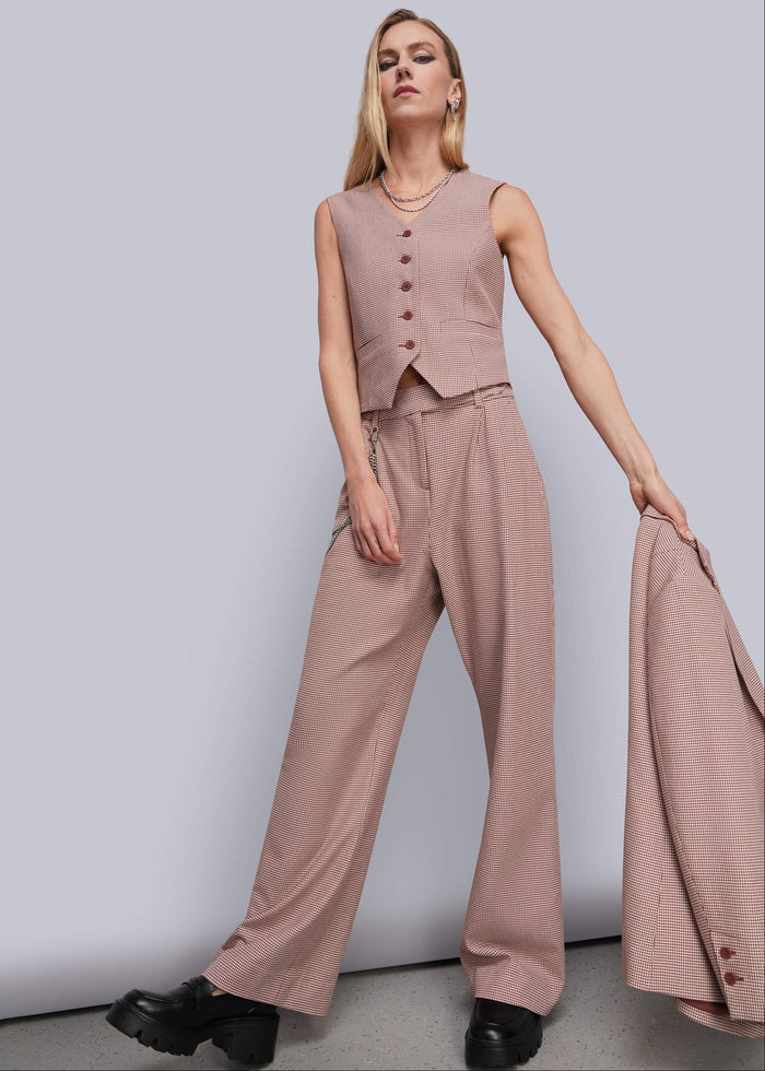 S=A woman models a sleeveless dusty red vest and matching wide-leg trousers, holding a matching blazer against a plain light gray studio background.