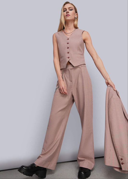S=A woman models a sleeveless dusty red vest and matching wide-leg trousers, holding a matching blazer against a plain light gray studio background.