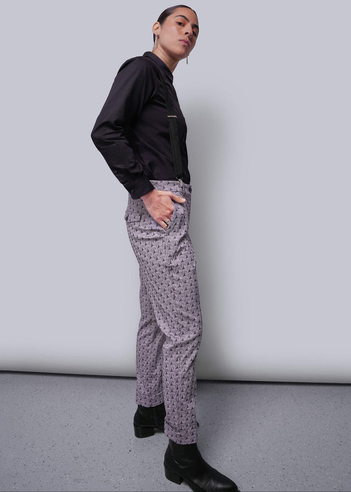 S=Person wearing a black shirt and patterned pants against a plain background