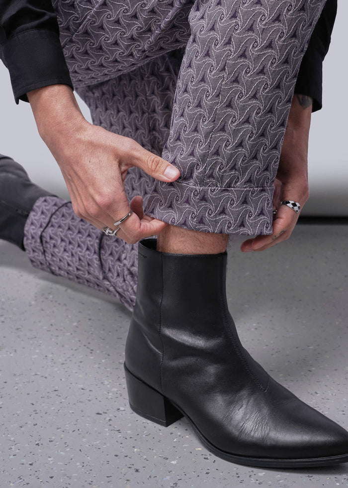 S=Person wearing black leather boots and purple patterned pants on a neutral background