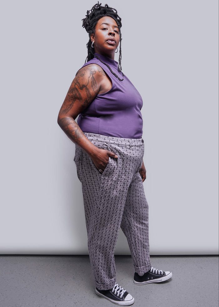 1X=Person wearing a purple sleeveless top and patterned pants against a plain background