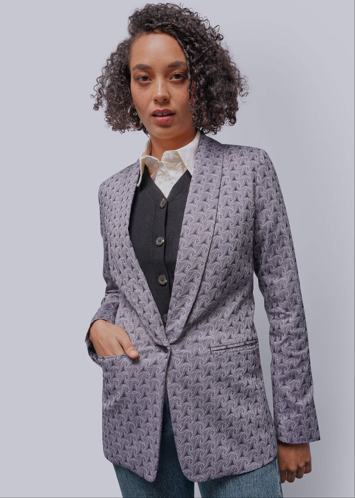 S=Woman wearing a purple patterned blazer over a shirt and vest on a plain background