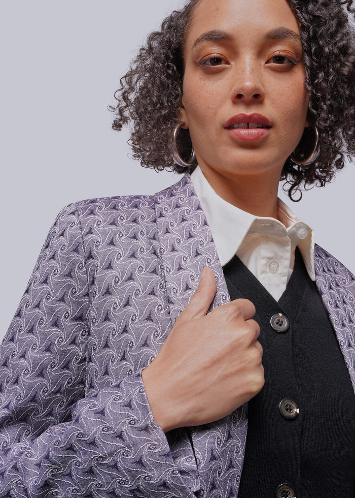 S=Person wearing a patterned jacket over a white shirt and black vest on a light gray background