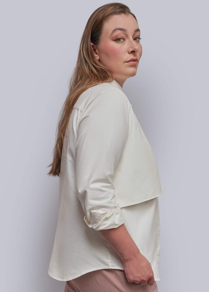 1X=A woman shown from the side and back wearing a white button up, set against a plain light gray studio background.