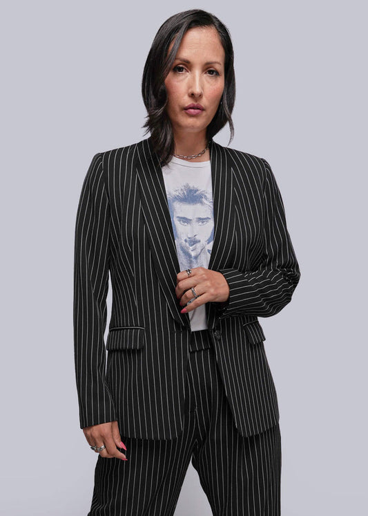 S=Woman wearing a black pinstripe suit over a light blue graphic t-shirt on a gray background