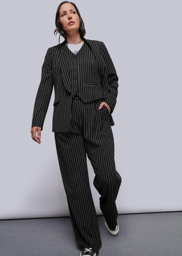 S=Person wearing a black pinstripe suit with sneakers on a plain background