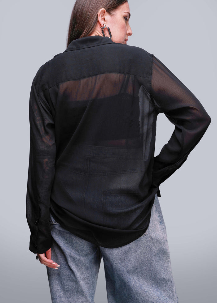 S=Person wearing a black sheer blouse with gray pants on a light gray background