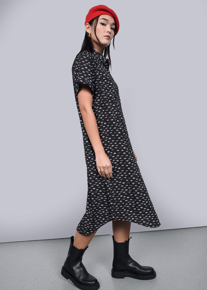 S=A person wearing a red beret, The Empower Shirt Dress in black with a subtle white pattern, and black boots poses confidently against a neutral background. The stylish dress features a modern button closure, completing the chic look.