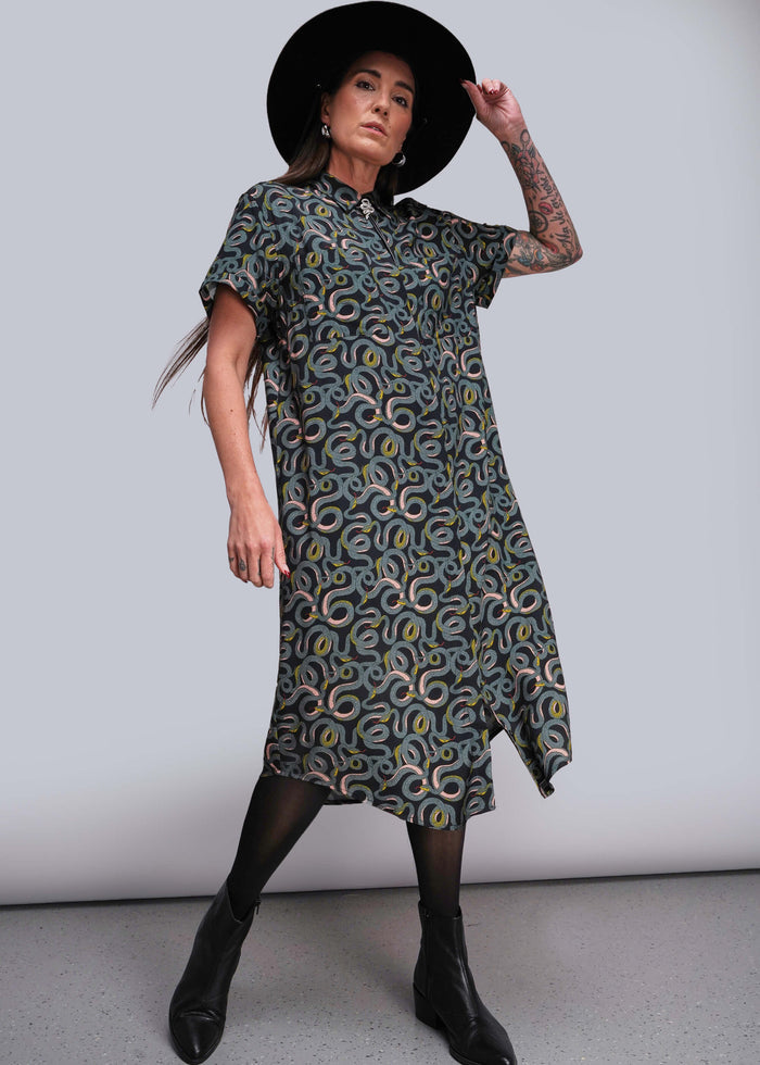 S=Woman wearing a patterned dress and black hat against a plain background