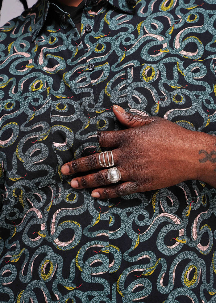 1X=Person wearing a patterned dress with a hand resting on it, showing jewelry.