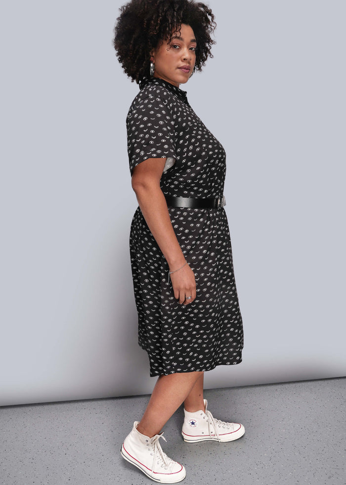 1X=Person wearing a black patterned dress with white sneakers on a plain background