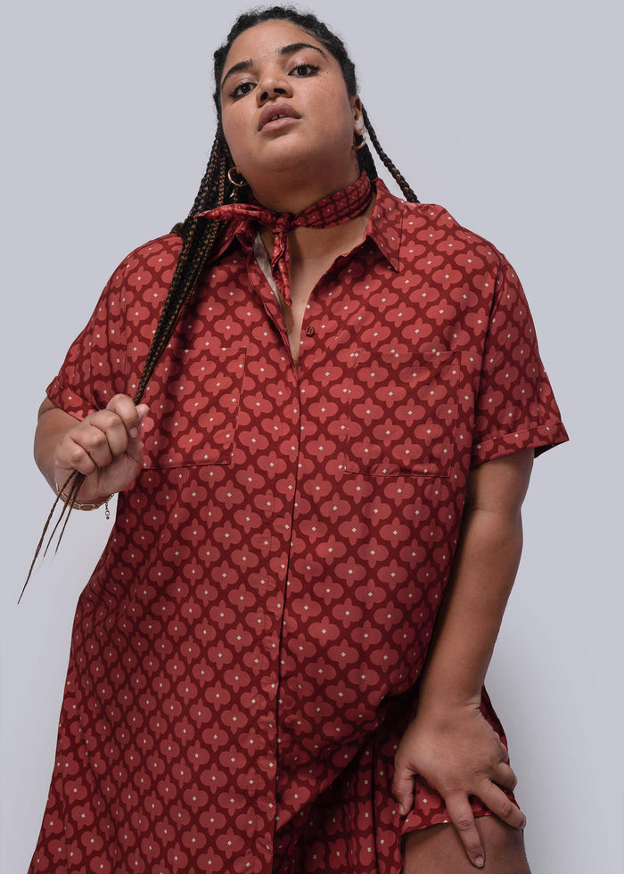 1X=Person wearing a red patterned dress and bandana against a plain background