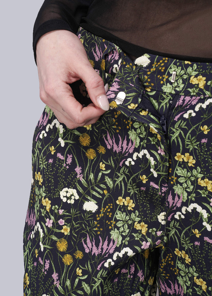 S=Floral-patterned pants with a hand adjusting the waistband against a neutral background