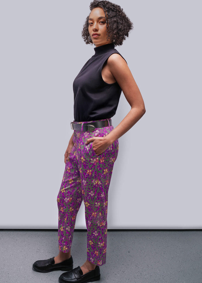 S=Woman wearing a black sleeveless top and purple floral pants against a gray background